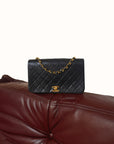 Black Chanel quilted handbag with gold chain on a brown leather couch