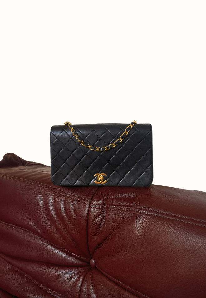 Black Chanel quilted handbag with gold chain on a brown leather couch